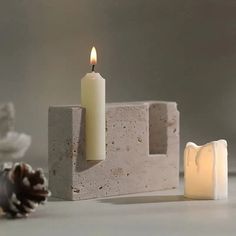 two candles sitting on top of cement blocks next to a pine cone and candle holder