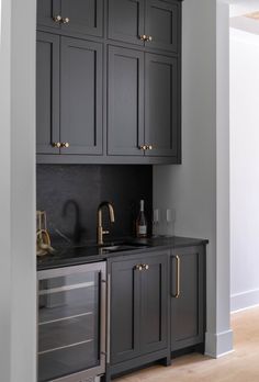 an empty kitchen with black cabinets and gold pulls on the cupboards in front of the sink