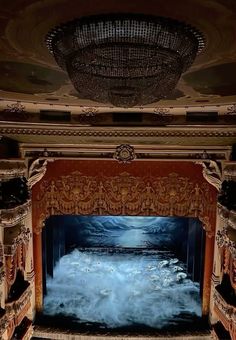 an empty theater with blue water on the stage and chandelier above it, as seen from the balcony