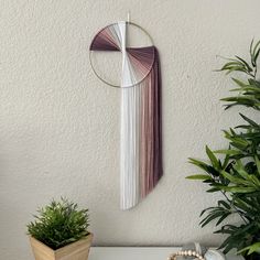 a wall hanging on the side of a white wall next to a potted plant