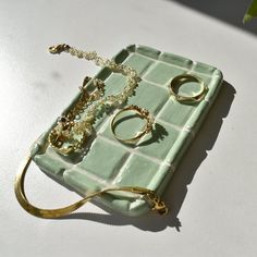 a tray with rings and bracelets sitting on top of a white table next to a plant