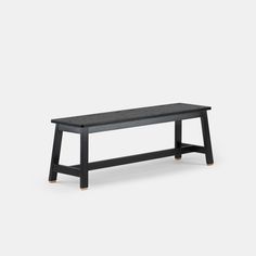 a black bench sitting on top of a white floor next to a wooden table with two legs