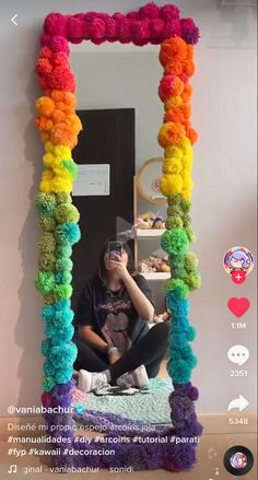 a woman taking a selfie in front of a colorful mirror with pom poms