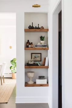 an open book shelf in the corner of a room with white walls and wood floors