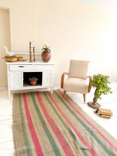 a room with a rug, chair and potted plant