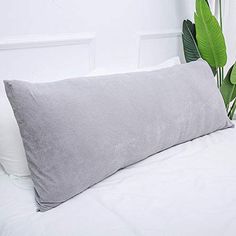 a large gray pillow sitting on top of a white bed next to a green plant