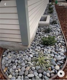 some rocks and plants are in a circular planter on the side of a house