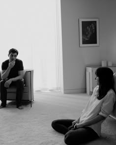 a man and woman sitting on the floor in front of a couch talking to each other