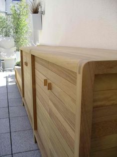 a wooden dresser sitting on top of a tiled floor next to a white wall and potted plant