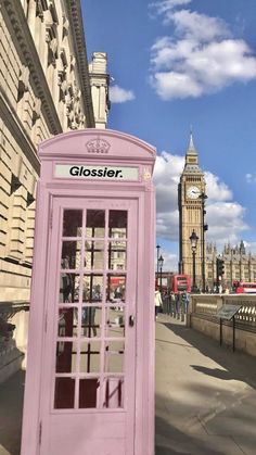 a pink phone booth stands in front of the big ben clock tower