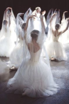 a group of women in white dresses are dancing on a stage with their arms outstretched