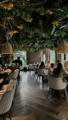 people sitting at tables in a restaurant with lots of greenery hanging from the ceiling