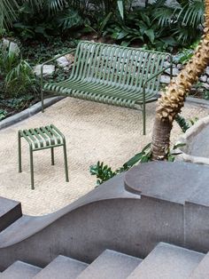 two green park benches sitting next to each other on top of a stone slab covered ground