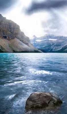 there is a rock in the middle of the water with mountains in the back ground