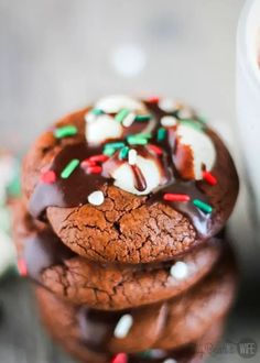 a stack of cookies with chocolate frosting and sprinkles next to a cup of coffee