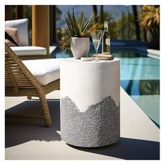 an outdoor table with two bottles and glasses on it next to a chair near a swimming pool