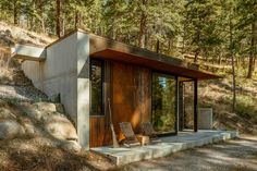 a small cabin in the woods with two chairs on the steps leading up to it