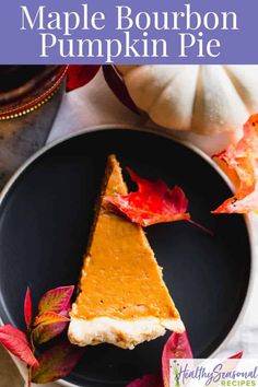 a slice of maple bourbon pumpkin pie on a black plate with autumn leaves around it