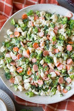 a bowl filled with broccoli, cauliflower and shrimp salad on top of a red checkered table cloth