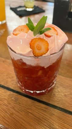 a drink with strawberries on the rim and garnished with leaves sits on a wooden table