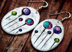 two white earrings with colorful designs on them sitting on top of a wooden table next to each other