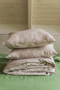 three pillows stacked on top of each other in front of a green bed sheet and wooden wall