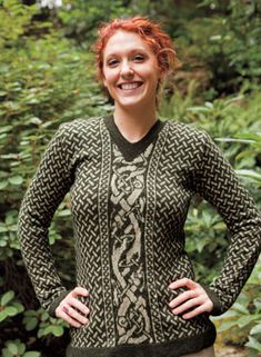 a woman standing in front of bushes wearing a sweater with an intricate design on it