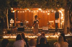 a woman playing guitar on stage in front of a group of people at an outdoor concert