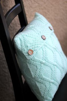 a green pillow sitting on top of a wooden chair next to a black chair cushion