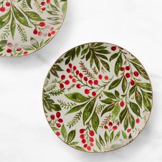 two plates with red berries and green leaves painted on them, sitting side by side