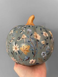 a hand holding a painted pumpkin with flowers on it