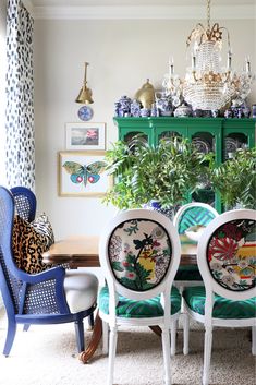 the dining room table is decorated with blue and white chairs, green china cabinet, and gold chandelier