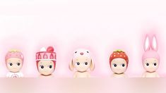 a row of little dolls with bunny ears and hats on their heads, in front of a pink background