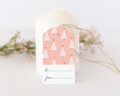 a white candle with a tag on it next to some pink and white christmas trees