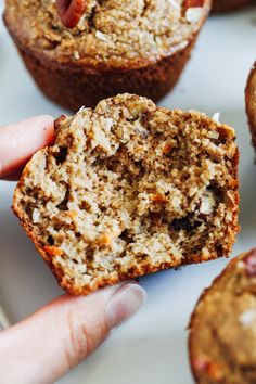 a person holding a muffin in their hand with other muffins behind it