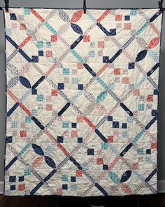 a quilt hanging on the side of a wall in front of a gray wall and wooden floor