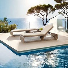 an empty lounge chair sitting on the edge of a swimming pool next to trees and water