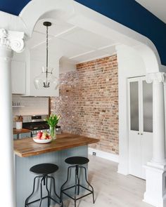 a kitchen with two stools next to an island and brick wall in the background