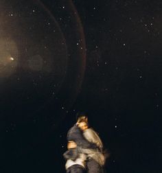 two people are standing in the dark with their arms around each other and looking up at the stars