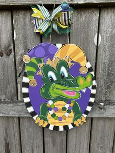 a green and purple dragon hanging from a wooden fence with a bow on it's head