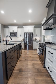 a kitchen with white cabinets and wood flooring, stainless steel appliances and black counter tops