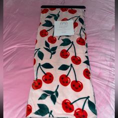 a blanket with cherries on it laying on a pink bed sheet that is folded up