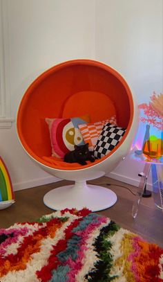 an orange egg chair sitting on top of a wooden floor next to a rainbow rug