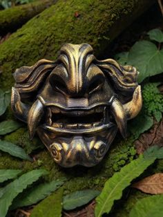 a close up of a mask on the ground near some green plants and mossy leaves