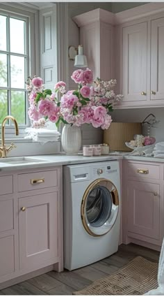 a kitchen with pink cabinets and flowers in a vase on the window sill next to a washing machine