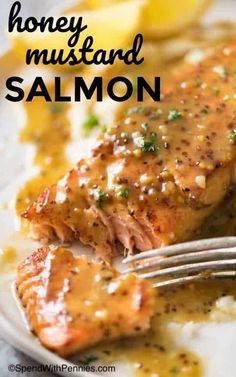 salmon with mustard sauce on a plate with a fork and lemon wedges next to it