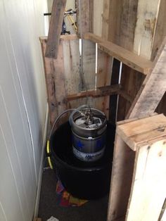 a bucket sitting on top of a black barrel next to a wooden wall and stairs