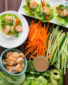 several plates and bowls filled with food on top of a wooden table next to lettuce