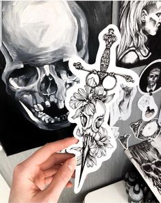 a person holding up a sticker in front of a skull and flower painting on a wall