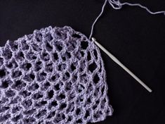 a crocheted hat with a knitting needle next to it on a black surface